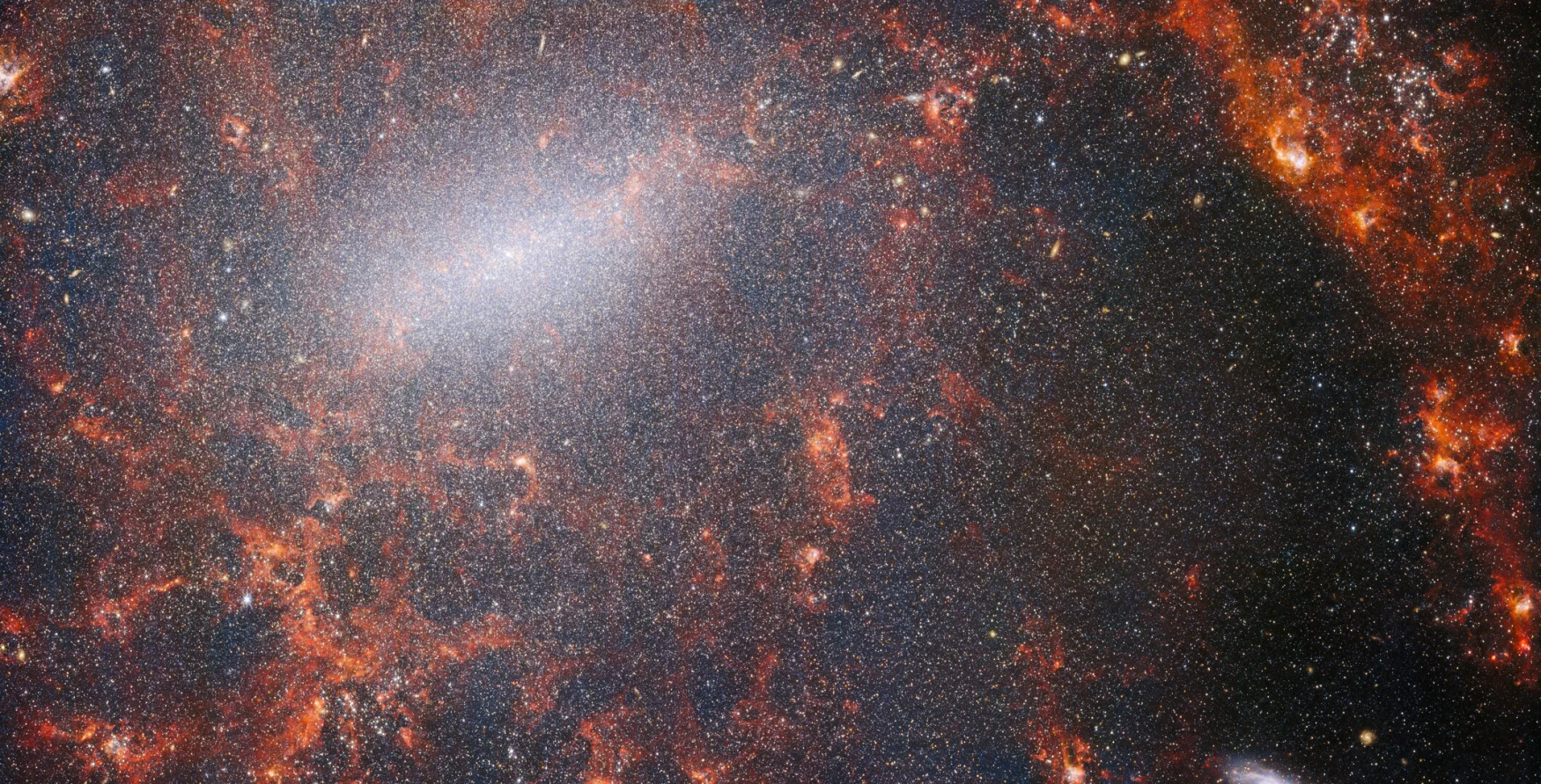 A delicate tracery of dust and bright star clusters threads across this image from the NASA/ESA/CSA James Webb Space Telescope. This view from WebbРђЎs NIRCam instrument is studded by the galaxyРђЎs massive population of stars, most dense along its bright central bar, along with burning red clouds of gas illuminated by young stars within. These glittering stars belong to the barred spiral galaxy NGC 5068, located around 17 million light-years from Earth in the constellation Virgo. This portrait of NGC 5068 is part of a campaign to create an astronomical treasure trove, a repository of observations of star formation in nearby galaxies. Previous gems from this collection can be seen here and here. These observations are particularly valuable to astronomers for two reasons. The first is because star formation underpins so many fields in astronomy, from the physics of the tenuous plasma that lies between stars to the evolution of entire galaxies. By observing the formation of stars in nearby galaxies, astronomers hope to kick-start major scientific advances with some of the first available data from Webb. The second reason is that WebbРђЎs observations build on other studies using telescopes including the NASA/ESA Hubble Space Telescope and some of the worldРђЎs most capable ground-based observatories. Webb collected images of 19 nearby star-forming galaxies which astronomers could then combine with catalogues from Hubble of 10 000 star clusters, spectroscopic mapping of 20├ѓ 000 star-forming emission nebulae from the Very Large Telescope (VLT), and observations of 12├ѓ 000 dark, dense molecular clouds identified by the Atacama Large Millimeter/submillimeter Array (ALMA). These observations span the electromagnetic spectrum and give astronomers an unprecedented opportunity to piece together the minutiae of star formation. This near-infrared image of the galaxy is filled by the enormous gathering of older stars which make up the core of NGC 5068. The keen vision of NIRCam allows astronomers to peer through the galaxyРђЎs gas and dust to closely examine its stars. Dense and bright clouds of dust lie along the path of the spiral arms: these are H II regions, collections of hydrogen gas where new stars are forming. The young, energetic stars ionise the hydrogen around them which, when combined with hot dust emission, creates this reddish glow. H II regions form a fascinating target for astronomers, and WebbРђЎs instruments are the perfect tools to examine them, resulting in this image. [Image Description: A close-in image of a spiral galaxy, showing its core and part of a spiral arm. At this distance thousands upon thousands of tiny stars that make up the galaxy can be seen. The stars are most dense in a whitish bar that forms the core, and less dense out from that towards the arm. Bright red gas clouds follow the twist of the galaxy and the spiral arm.] Links NGC 5068 (NIRCam+MIRI Image) NGC 5068 (MIRI Image) Slider Tool (MIRI and NIRCam images) Video: Pan of NGC 5068 Video: Webb's views of NGC 5068 (MIRI and NIRCam images) Video: Zoom into NGC 5068 