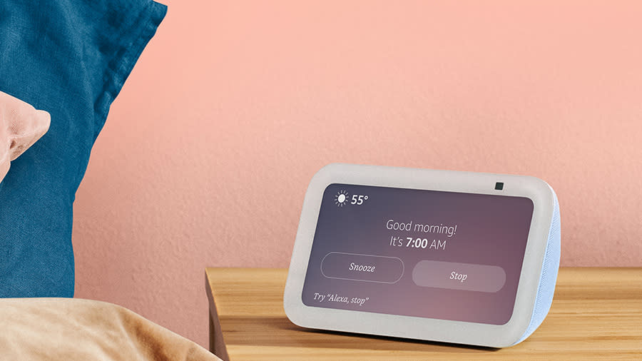 The echo show 5 smart display sits on a night stand in a room painted bright pink. The display reads 